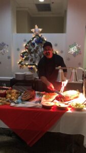 Chef, Pepe, stands behind a spread of our Prime Rib, Glazed Ham, and Charcuterie in the Esplanade Gardens dining room.